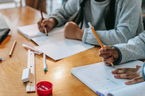 Free Crop pupils writing in copybook on desk Stock Photo